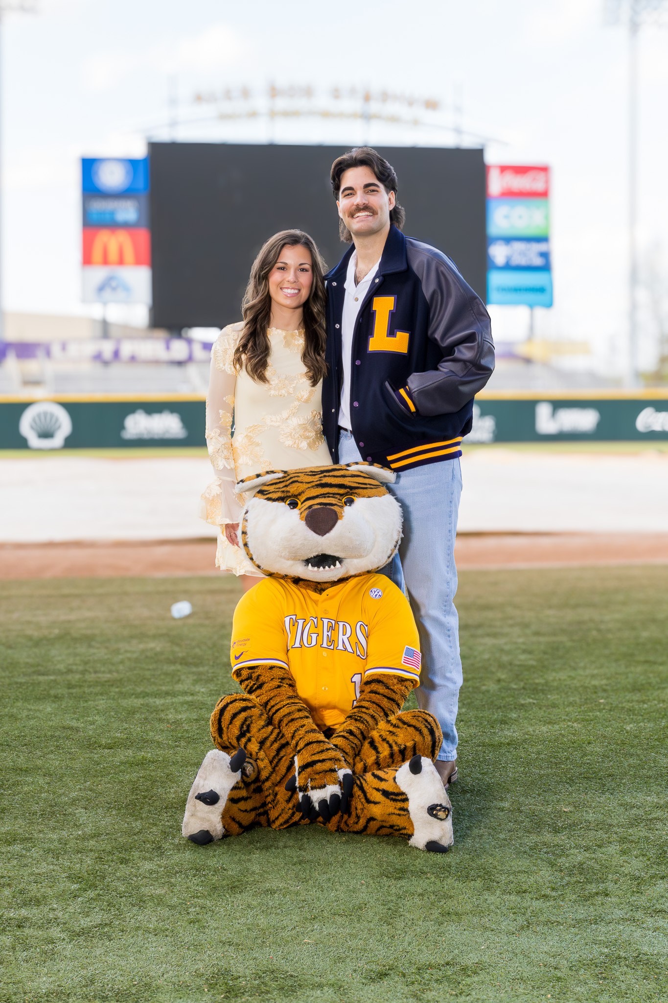 Landon Terro poses with his girlfriend on the field at Alex Box Stadium alongside Mike the Tiger during a graduation photo session.