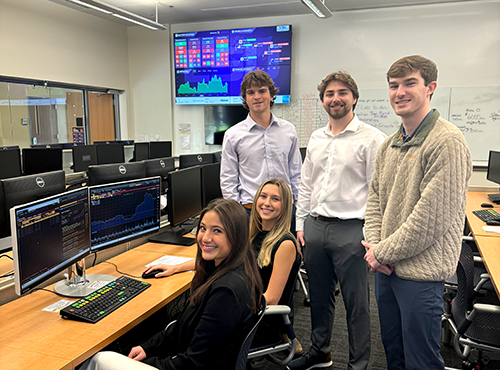 2024 Bloomberg team gathered around computers in the SMART Lab, they are in professional attire.