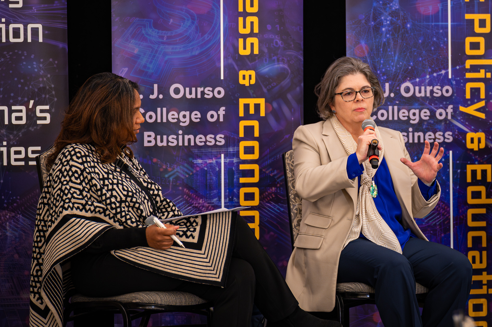 Two women speaking on stage while sitting in chairs. 