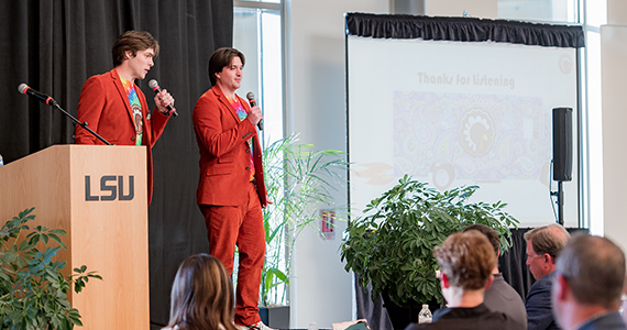 Two students in vibrant cordaroy suits pitch their business stage.