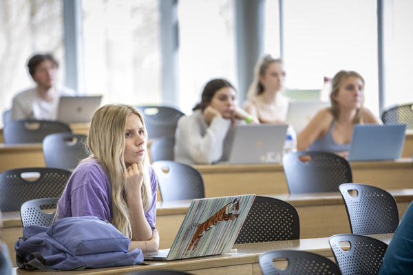 Female student listens attentively in classroom with laptop on desk.