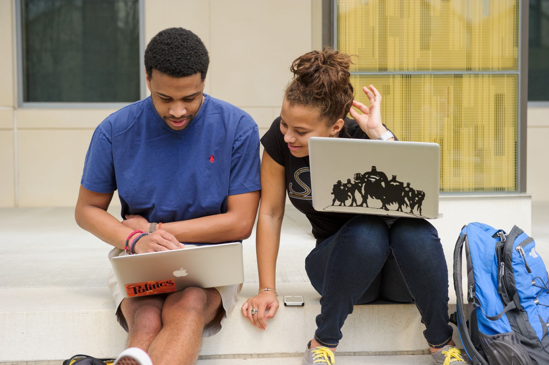 Two students with computers in their lap sitting outside.